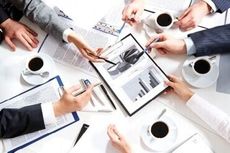 Reunião de negócios em torno de uma mesa, com pessoas analisando gráficos e documentos. Xícaras de café presentes.