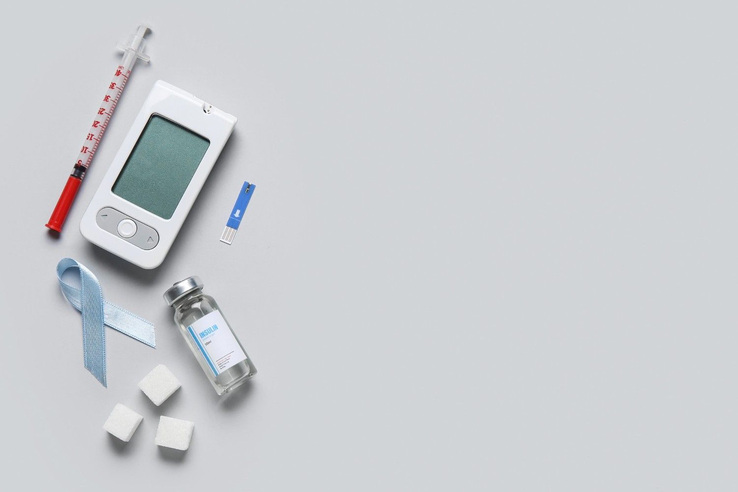 Elementos para el cuidado de la diabetes sobre fondo gris: monitor de glucosa, jeringa de insulina