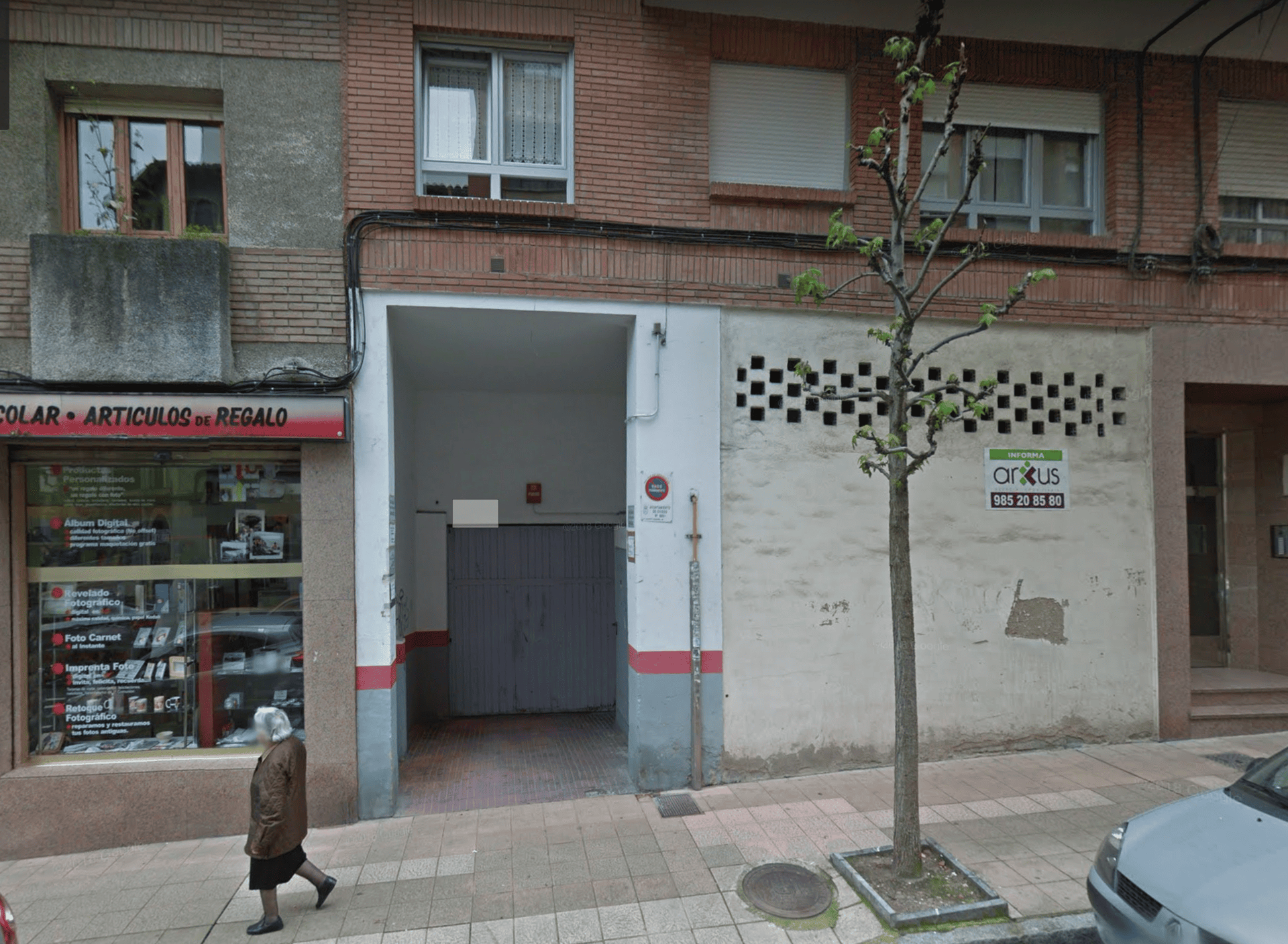 Vista de la calle: Entrada a un edificio con una tienda a la izquierda, una entrada abierta y un peatón en la acera.