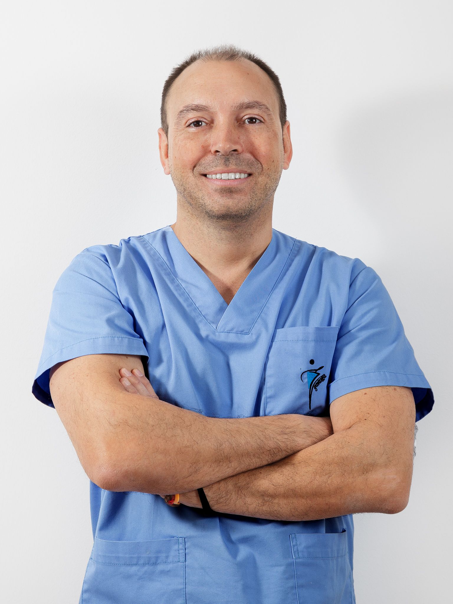 Un hombre con una blusa azul está de pie con los brazos cruzados y sonriendo.