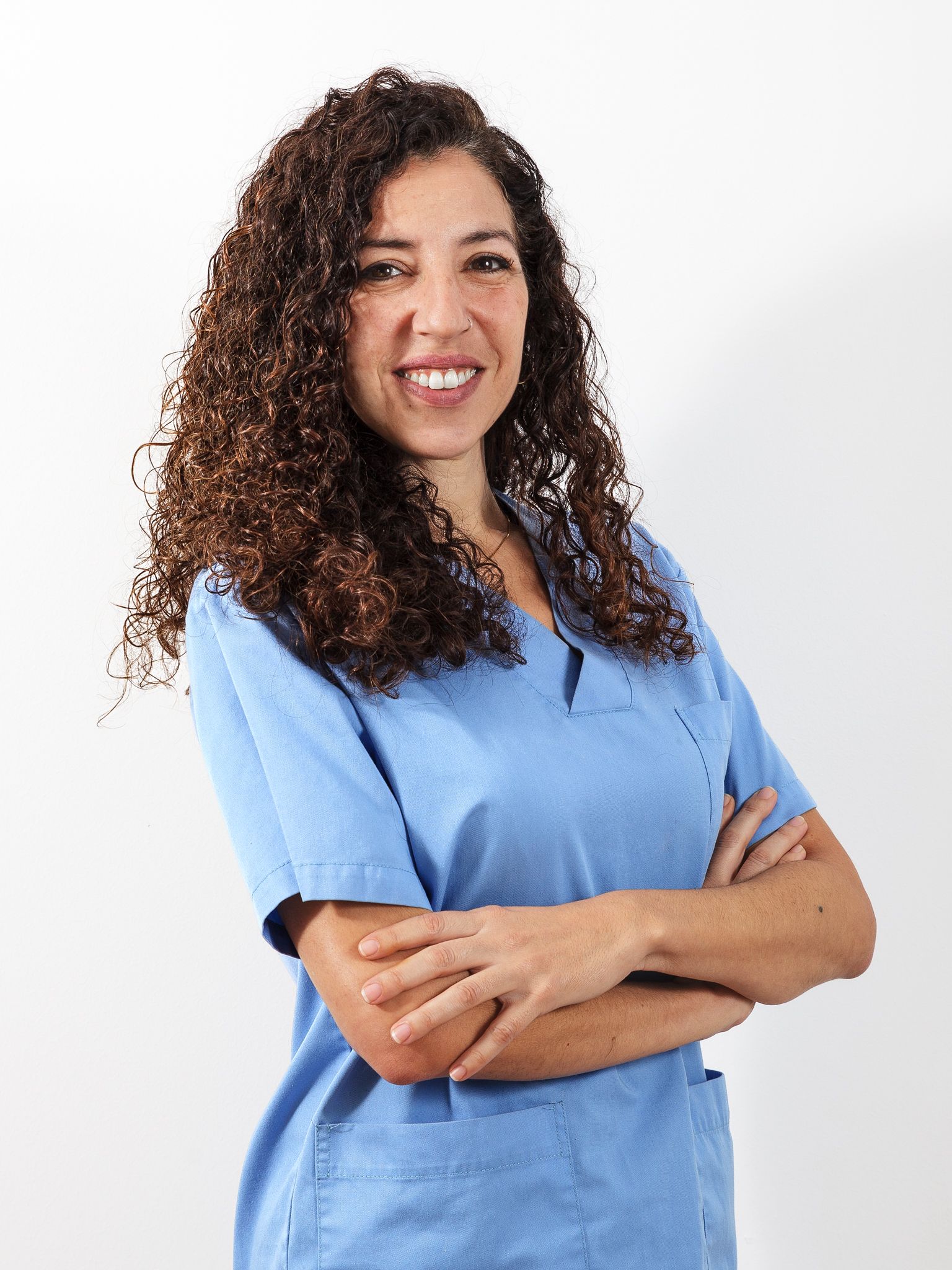 Una mujer con una blusa azul está de pie con los brazos cruzados y sonriendo.