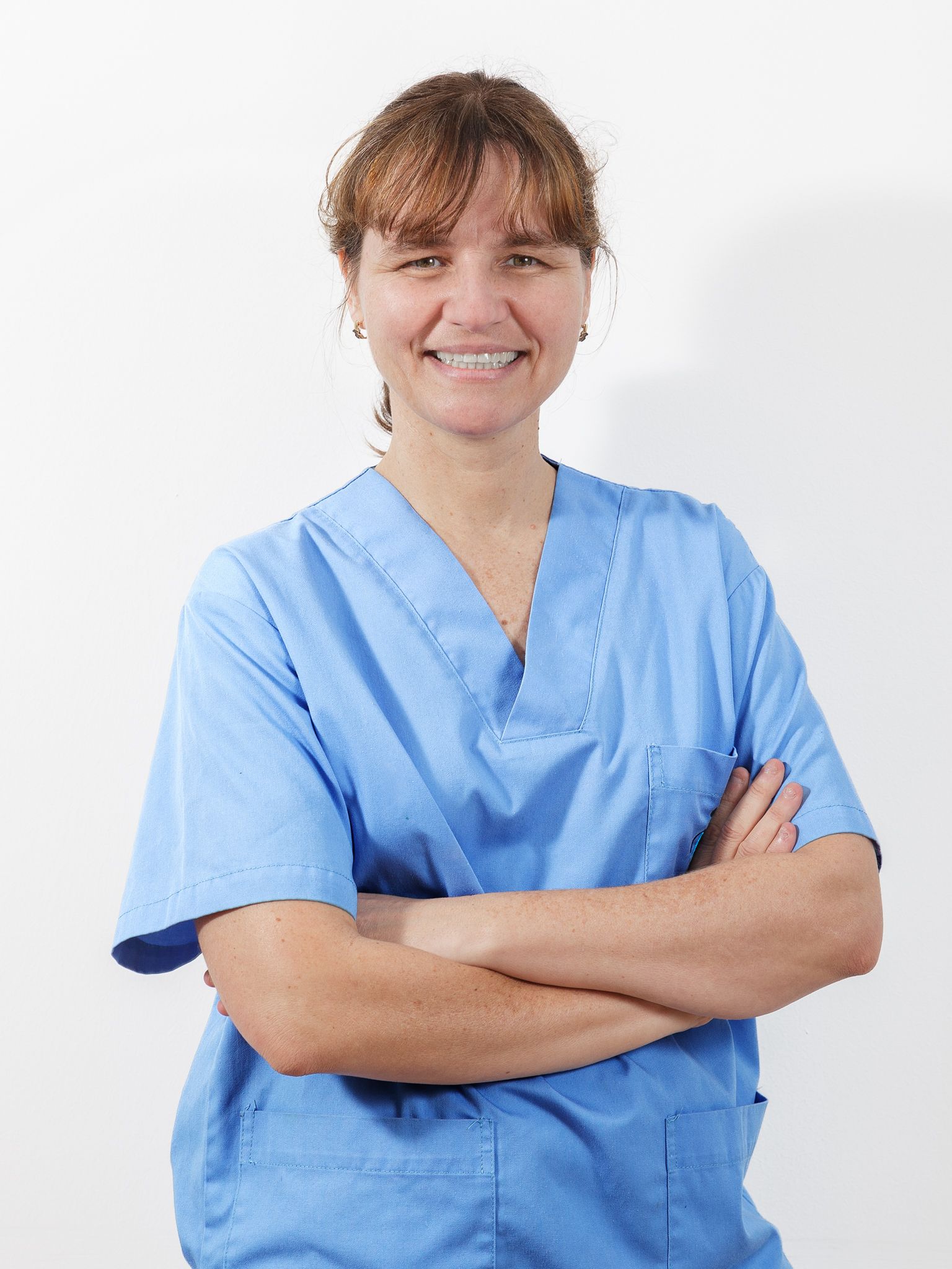 Una mujer con un uniforme azul está de pie con los brazos cruzados y sonriendo.