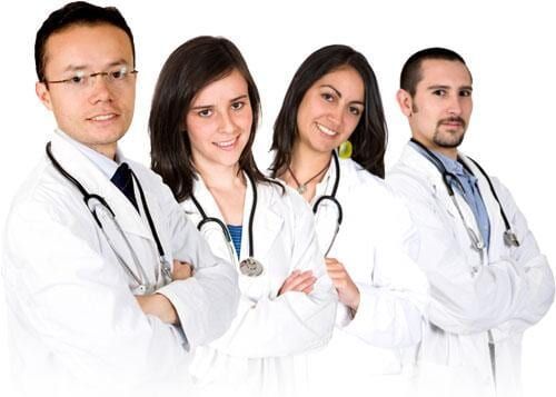 Quatro médicos, de aparência diversa, sorriem com os braços cruzados, vestindo jalecos brancos e estetoscópios.