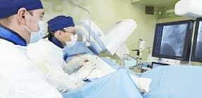 Médicos realizando um procedimento médico em uma sala de cirurgia estéril, observando monitores.