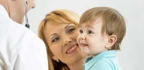 Um médico ausculta o peito de um bebê segurado pela mãe. O bebê sorri.