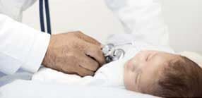 Médico examinando o peito de um bebê dormindo com um estetoscópio.