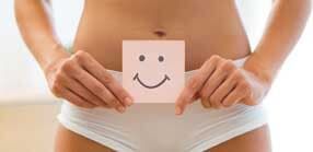 Mulher segurando um cartão com um rosto sorridente sobre a calcinha, promovendo a saúde vaginal.