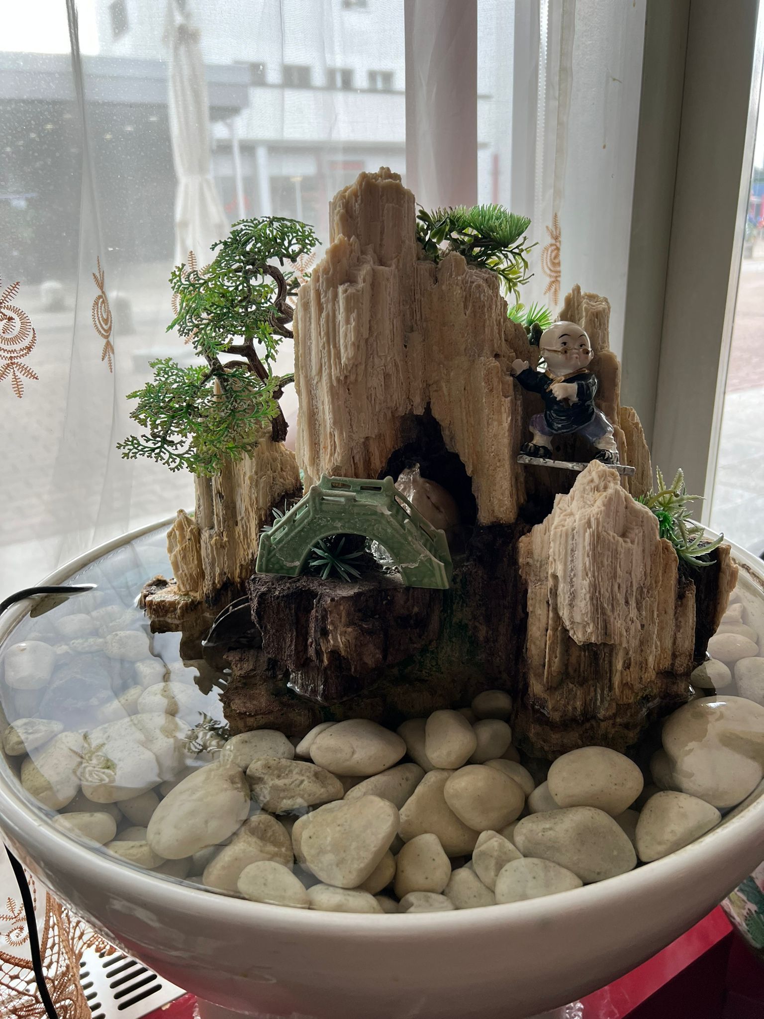 Auf einem Tisch vor einem Fenster steht eine mit Steinen und Pflanzen gefüllte Schüssel.