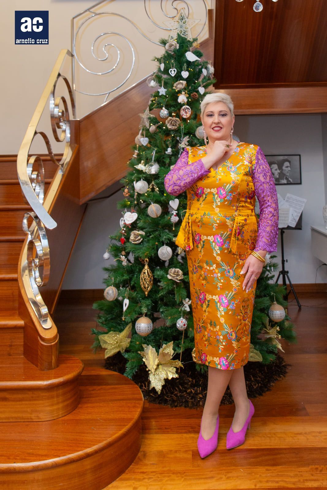 Mujer con vestido floral, tacones rosas, posa cerca del árbol de Navidad y la escalera.