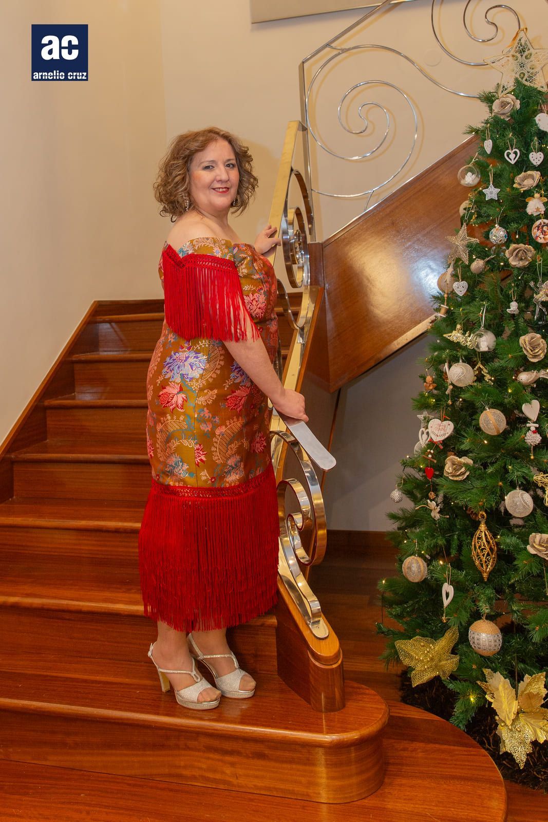 Mujer con vestido festivo posa en las escaleras cerca de un árbol de Navidad.