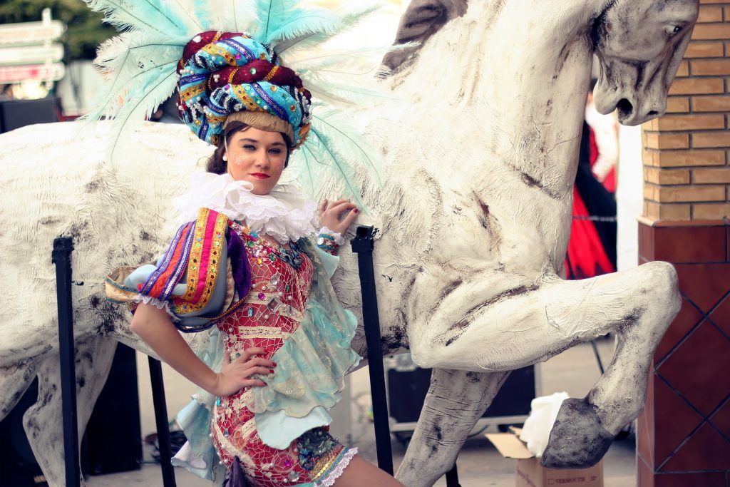 Una mujer con un traje colorido está de pie junto a una estatua de un caballo.