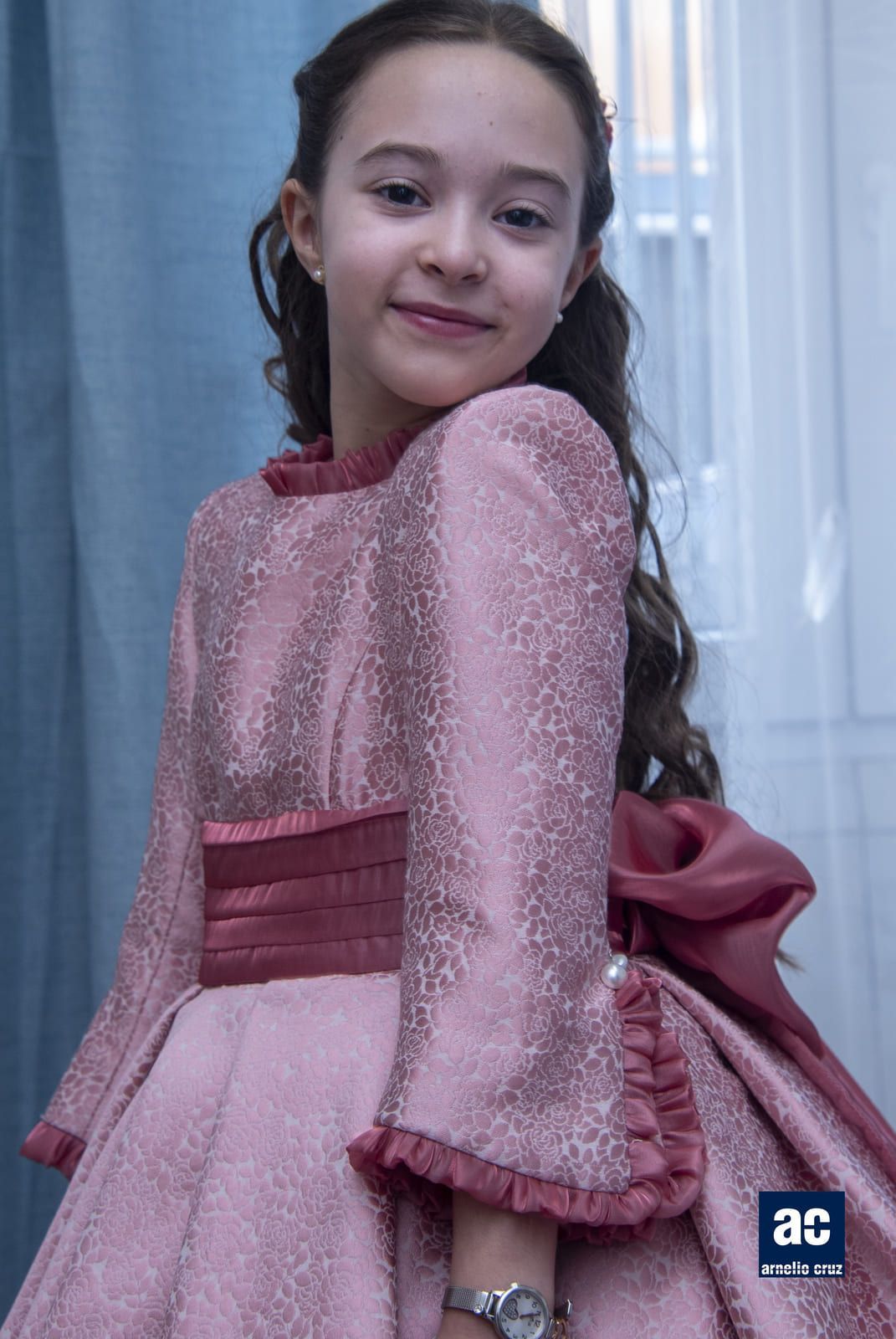 Niña con un vestido rosa, sonriendo, en el interior.