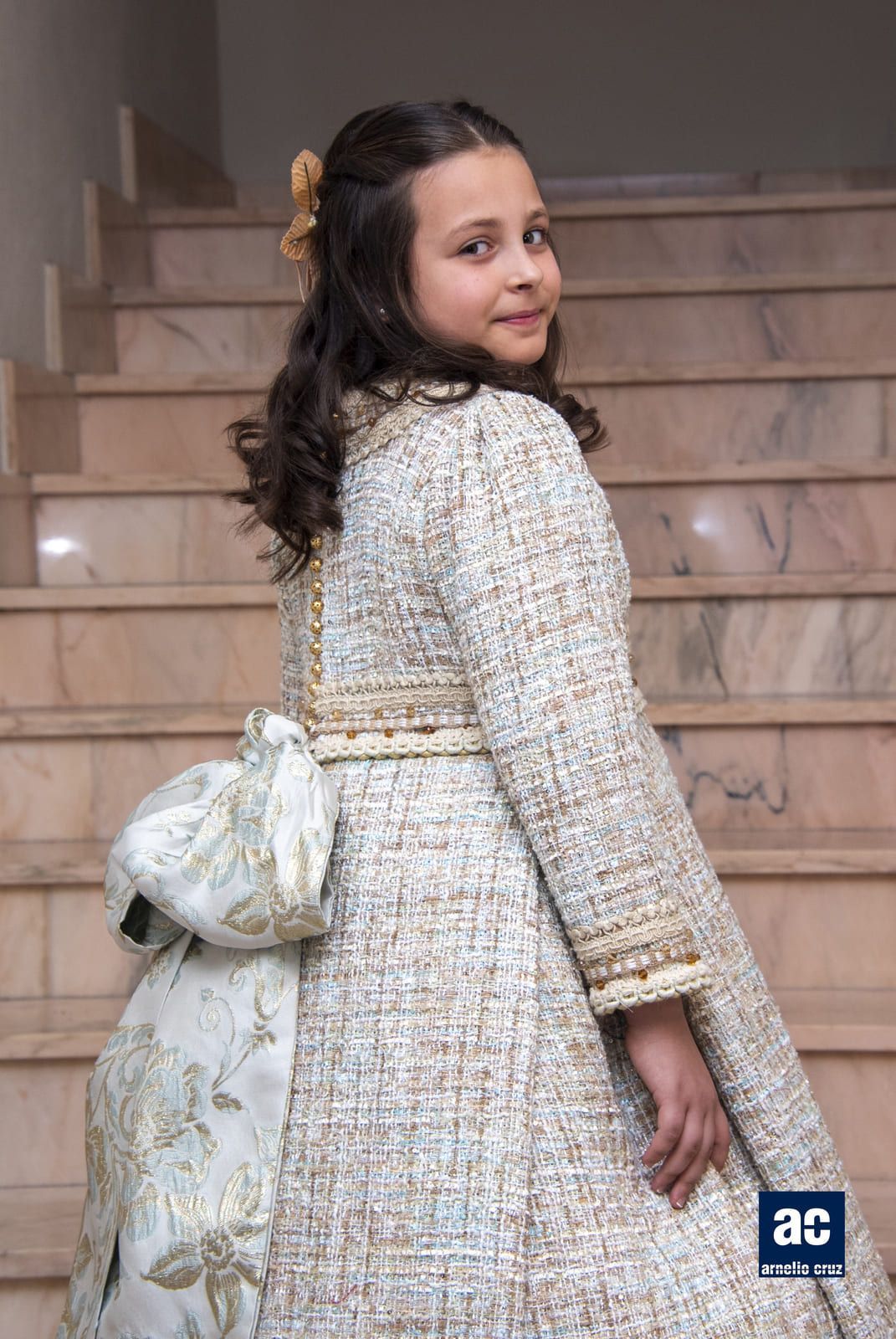 Persona joven con un abrigo de tweed y un lazo, de pie en una escalera de mármol.