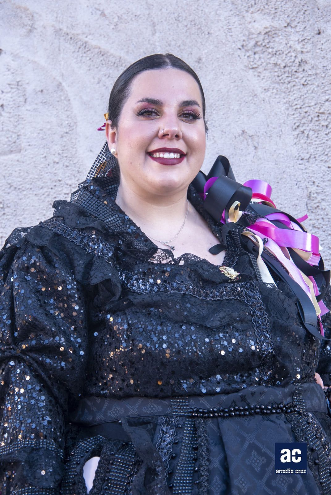 Mujer con traje tradicional de encaje negro, sonriendo, sosteniendo cintas.