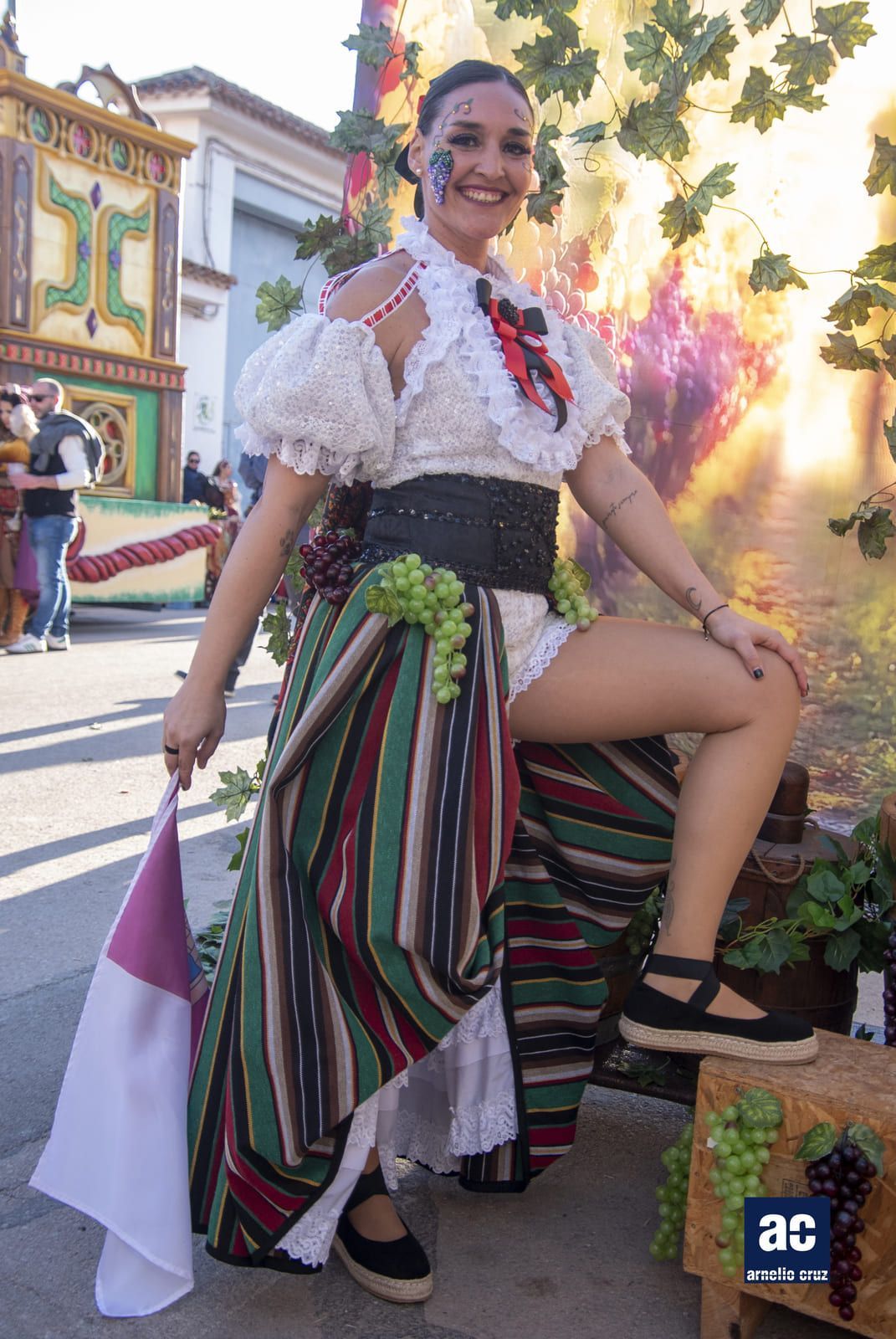 Mujer disfrazada posa con bandera, uvas y un fondo de vides.