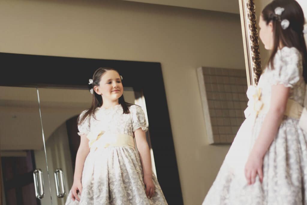 Una chica con un vestido blanco está parada frente a un espejo.