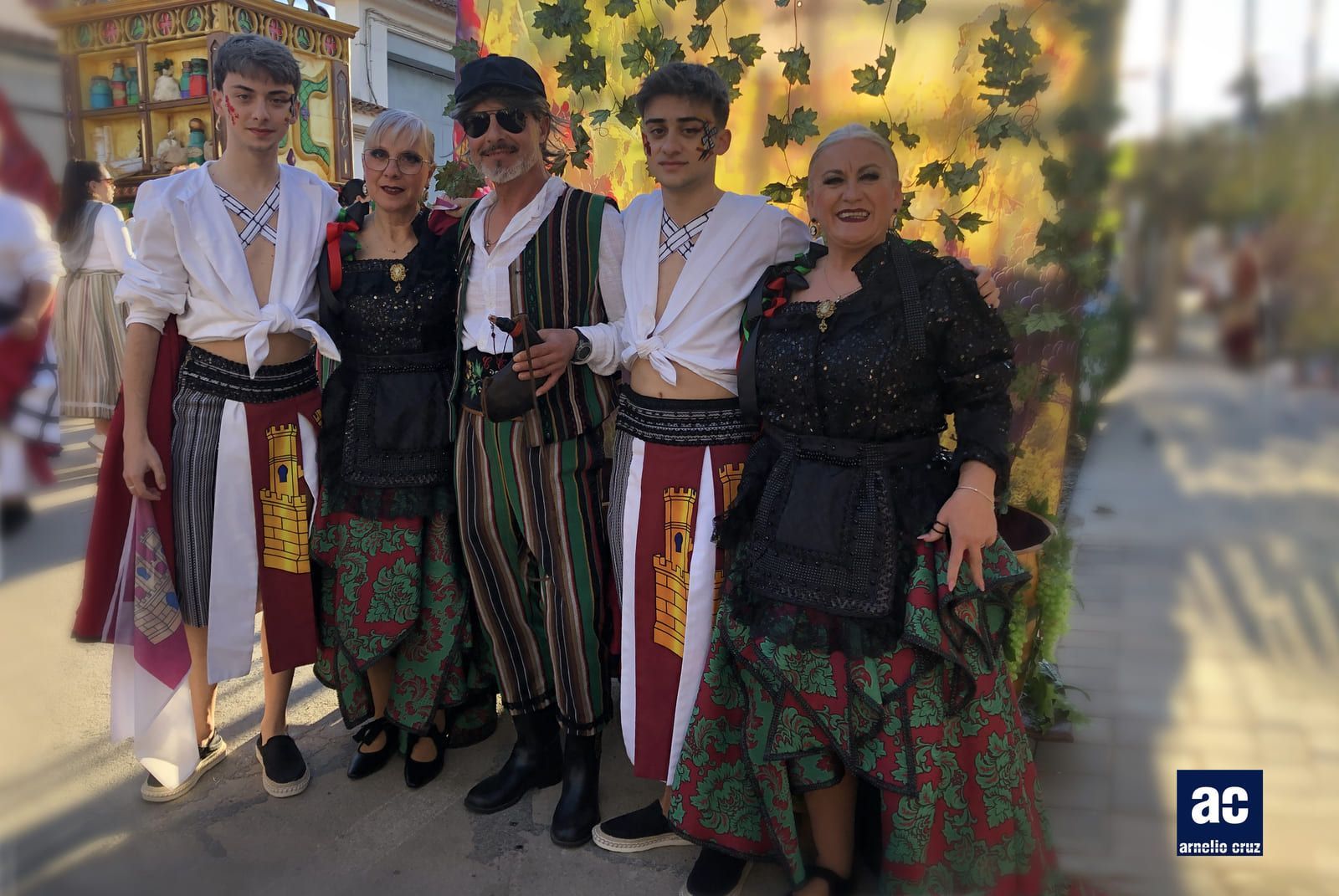 Grupo de cinco personas posando con trajes tradicionales, con un fondo ornamentado.