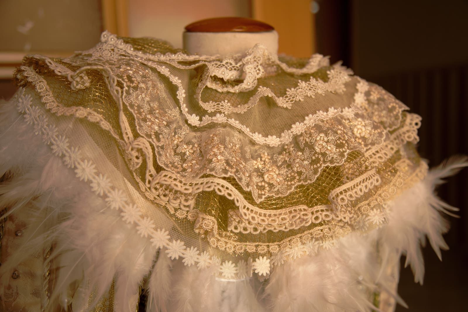 Cuello de encaje y plumas en un maniquí. Tonos crema y dorado con detalles intrincados.