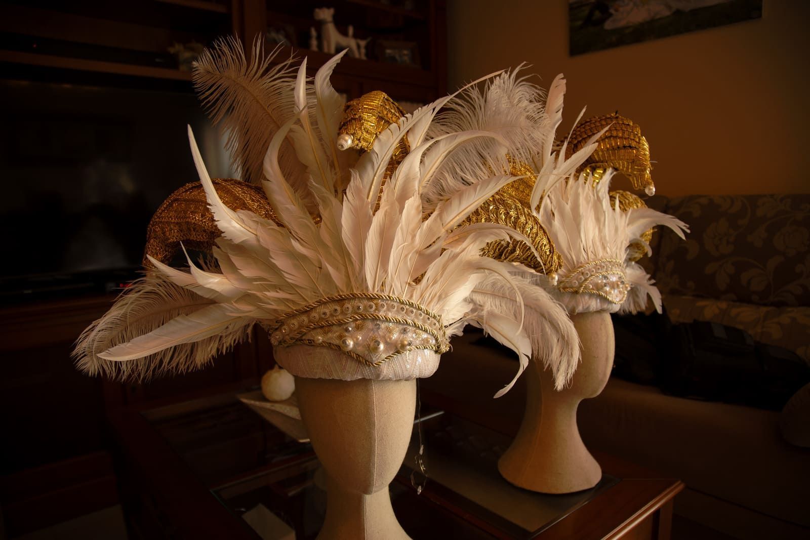 Dos elaborados tocados de plumas blancas con detalles dorados exhibidos en cabezas de maniquí, en el interior.