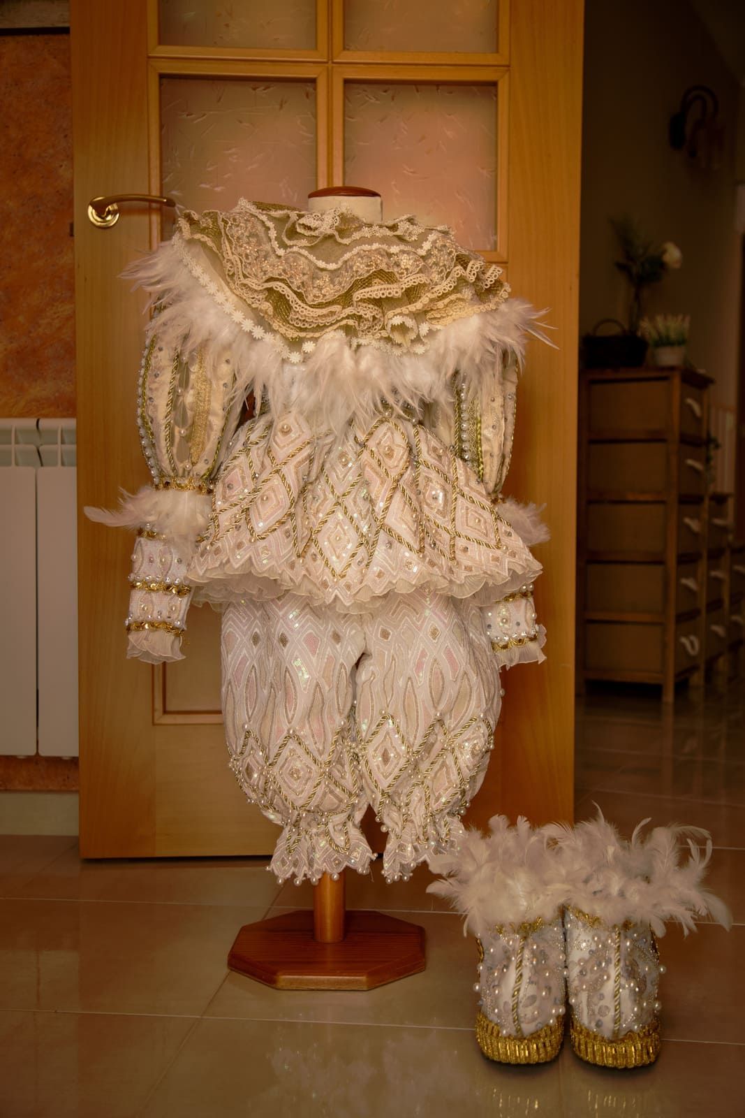 Traje adornado en color crema y dorado sobre un maniquí con botas a juego; puerta al fondo.
