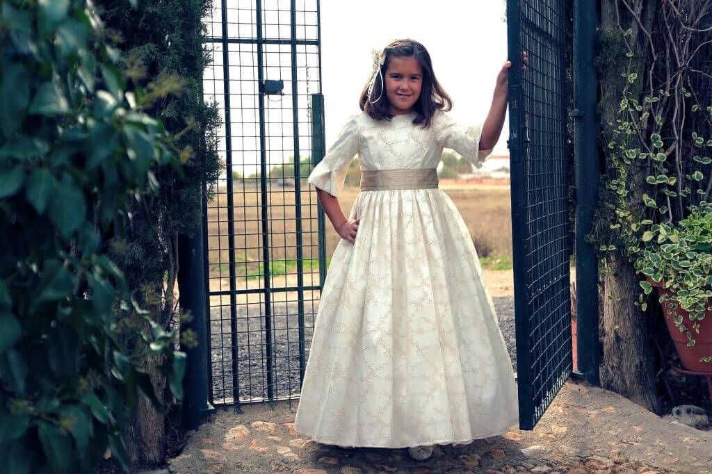 Una niña con un vestido blanco está parada frente a una puerta.