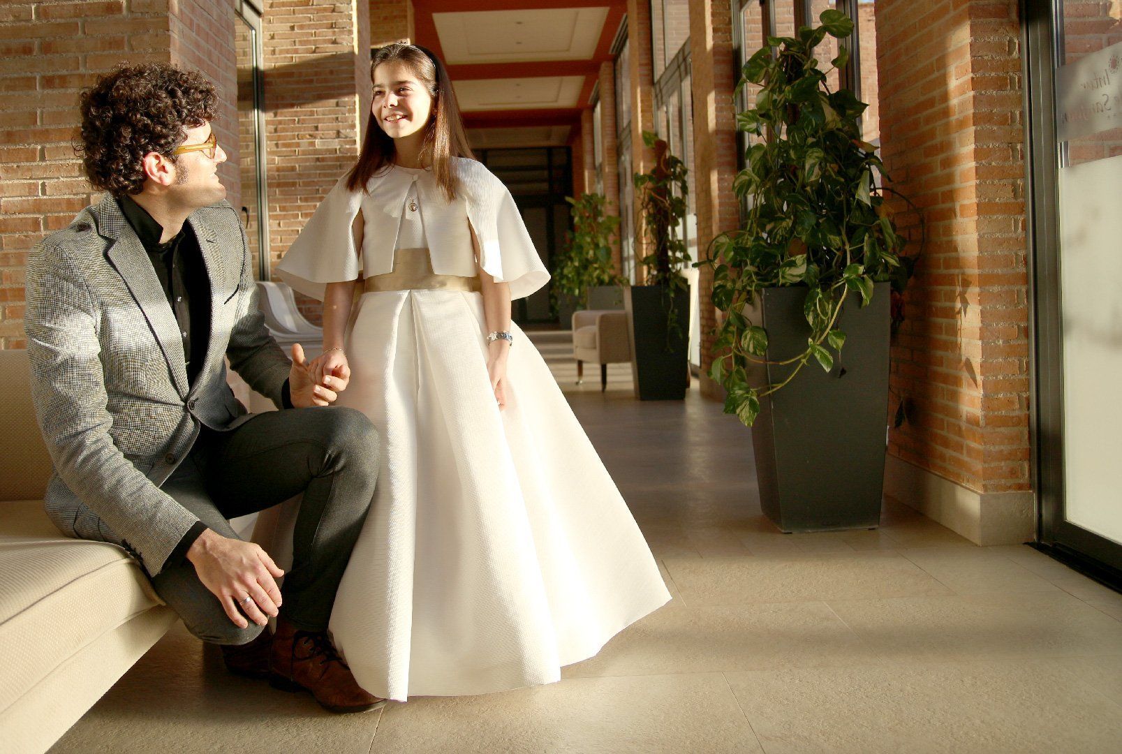 Un hombre está sentado en un sofá junto a una chica con un vestido blanco.