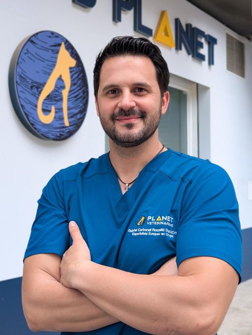 Hombre con uniforme médico azul, con los brazos cruzados y sonriendo. El logo de la camiseta dice 