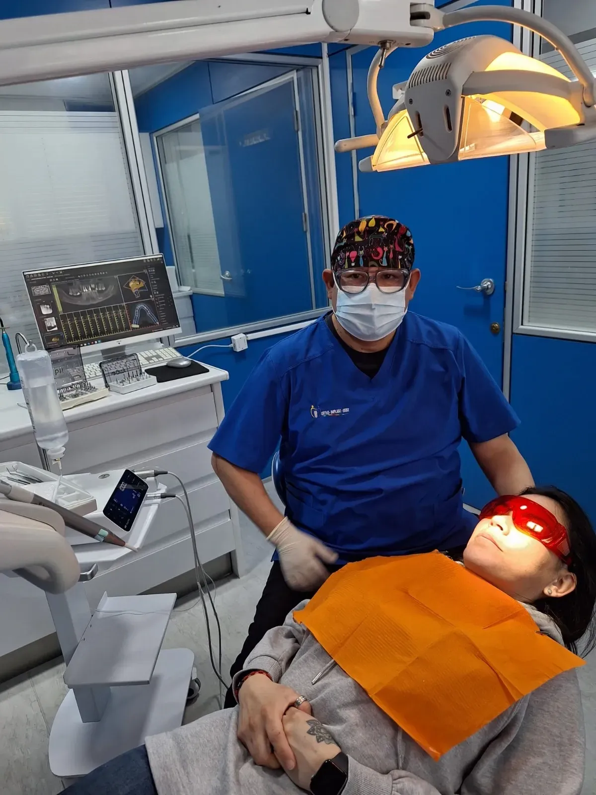 Un hombre con una máscara está de pie junto a una mujer en una silla dental.