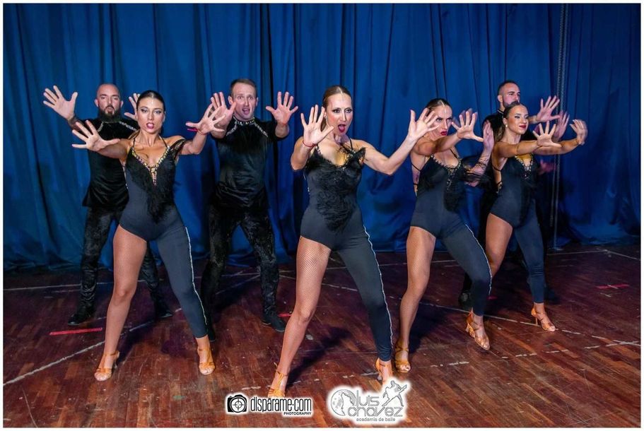 Un grupo de personas está bailando en un escenario frente a una cortina azul.