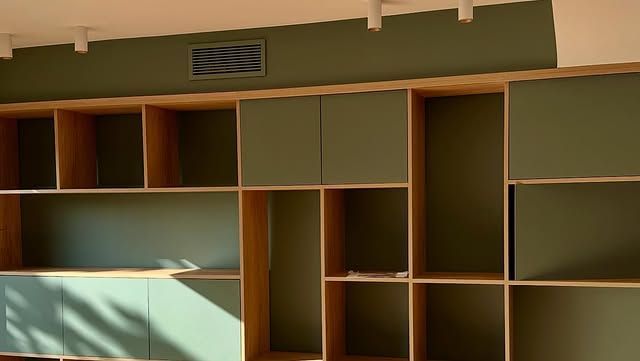 Étagères encastrées en bois vides dans une pièce baignée de lumière naturelle et jouant avec les ombres.