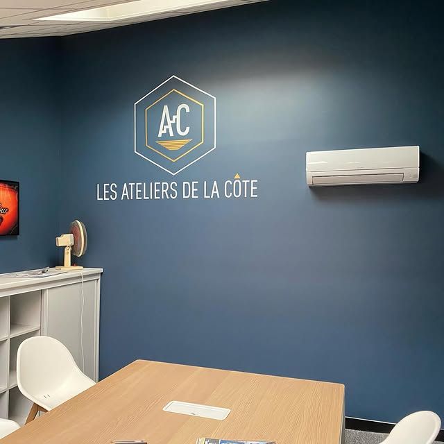 Salle d'attente bleue avec logo AC et enseigne murale Les Ateliers de la Côte, table et chaises.