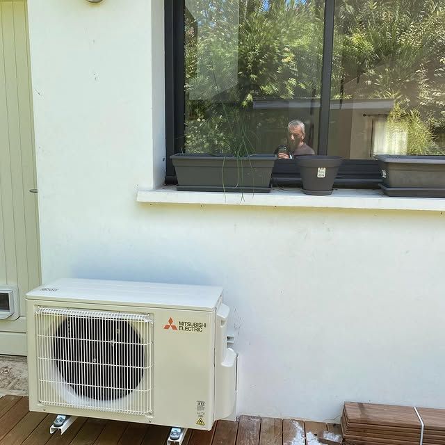 Mur blanc avec un climatiseur sous une fenêtre reflétant une personne à l'intérieur.
