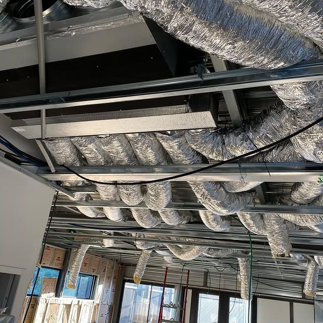 Plafond apparent avec conduits de ventilation argentés et charpente métallique dans un bâtiment en construction.
