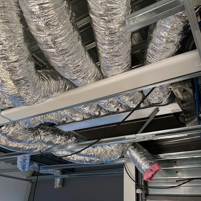 Conduits de ventilation au plafond avec tubes isolés argentés et structure métallique apparente dans un bâtiment en construction.