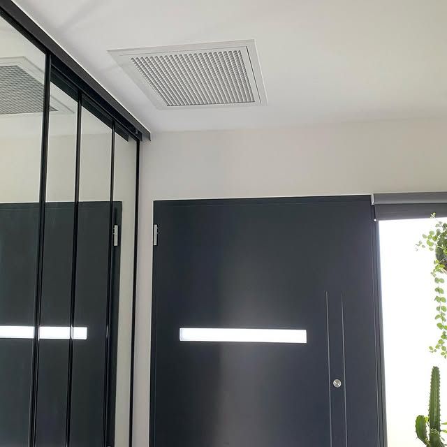 Intérieur moderne avec portes noires, placard à miroirs, grille d'aération blanche au plafond et un cactus près d'une porte ouverte.