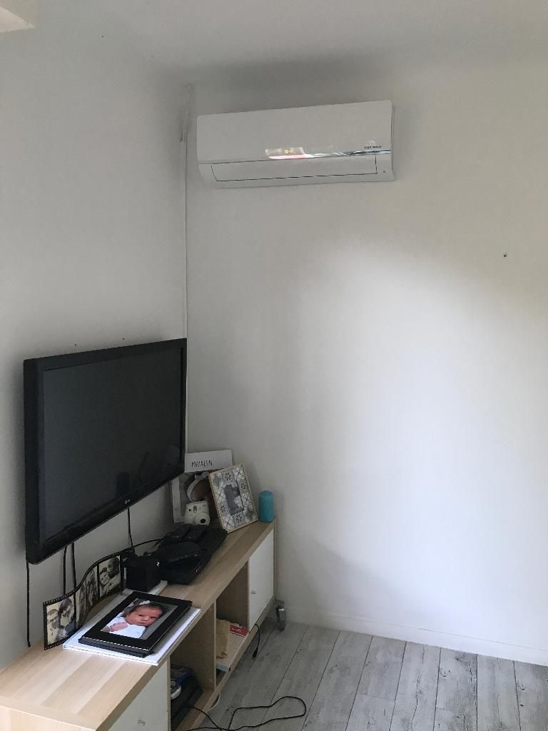 Petite pièce avec une télévision fixée au mur, une étagère et un climatiseur sur un mur blanc.