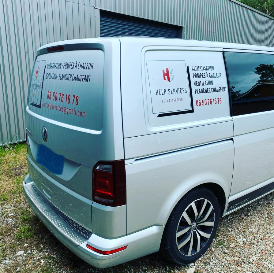 Une camionnette blanche portant les couleurs de l'entreprise est garée à côté d'un bâtiment en tôle ondulée.