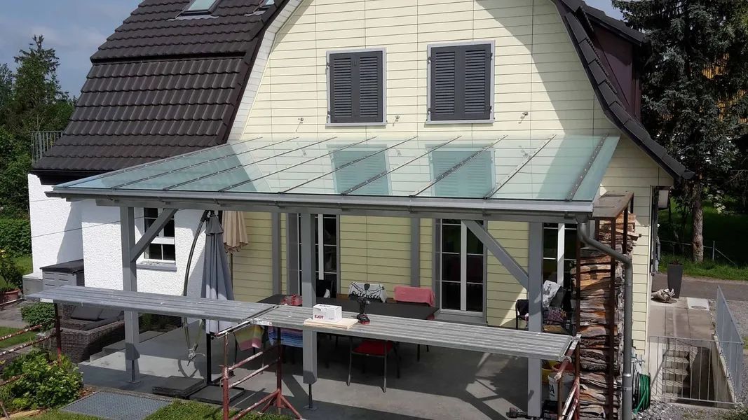 Ein grosses weisses Haus mit einer Pergola mit Glasdach. Foto von der Mannhart Holzbau AG