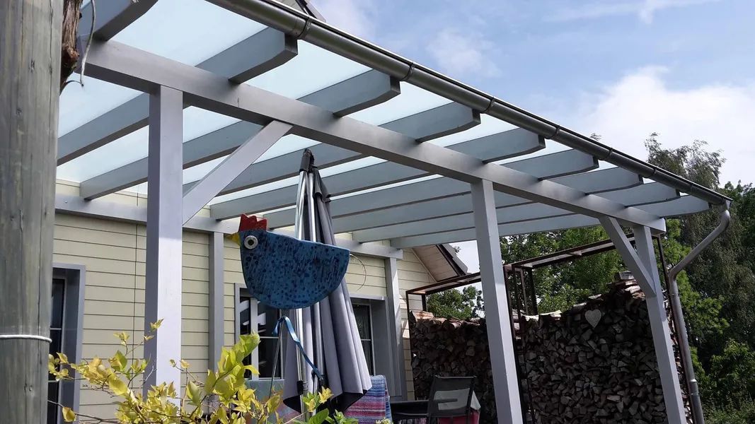 Ein blaues Huhn hängt an einer Pergola vor einem Haus. Foto von der Mannhart Holzbau AG