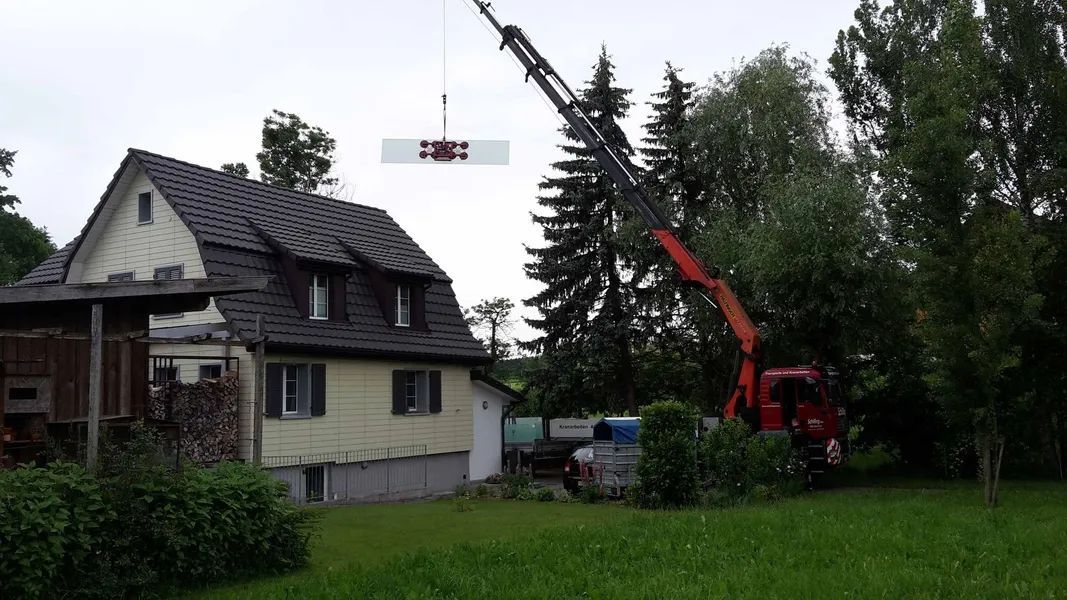 Ein Kran hebt ein großes Stück Holz über ein Haus.