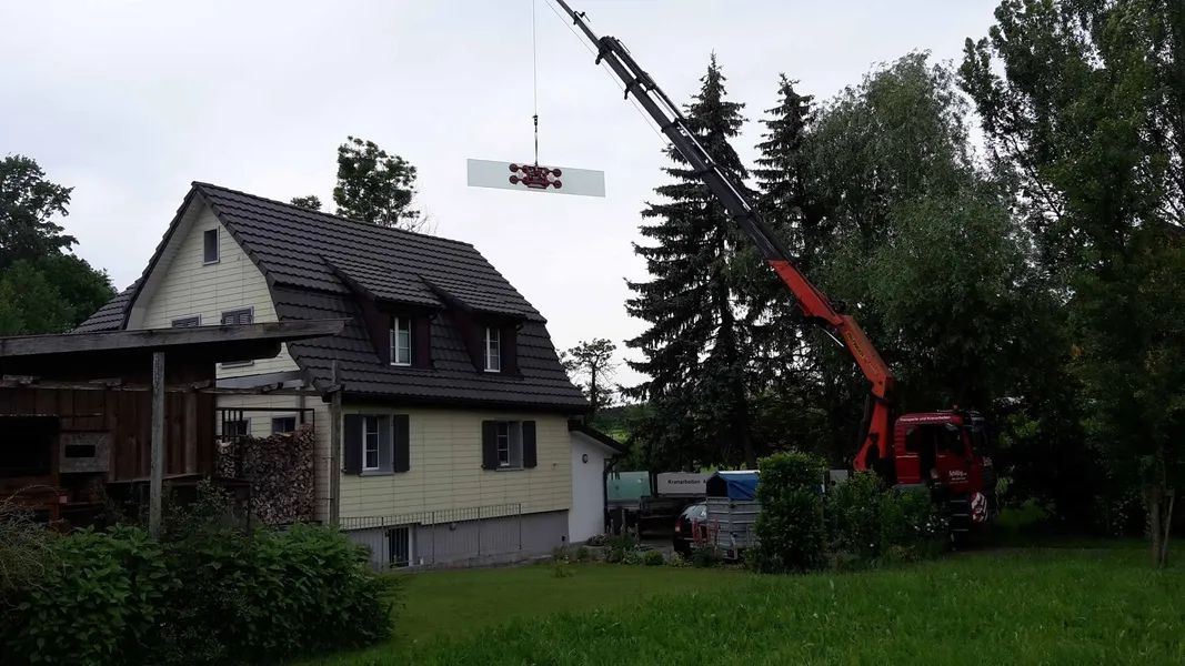 Ein Kran hebt ein Stück Holz vor einem Haus an. Foto von der Mannhart Holzbau AG