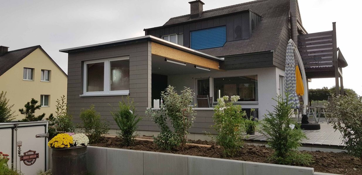 Ein grosses Haus mit vielen Fenstern ist von Bäumen und Büschen umgeben. Foto von der Mannhart Holzbau AG