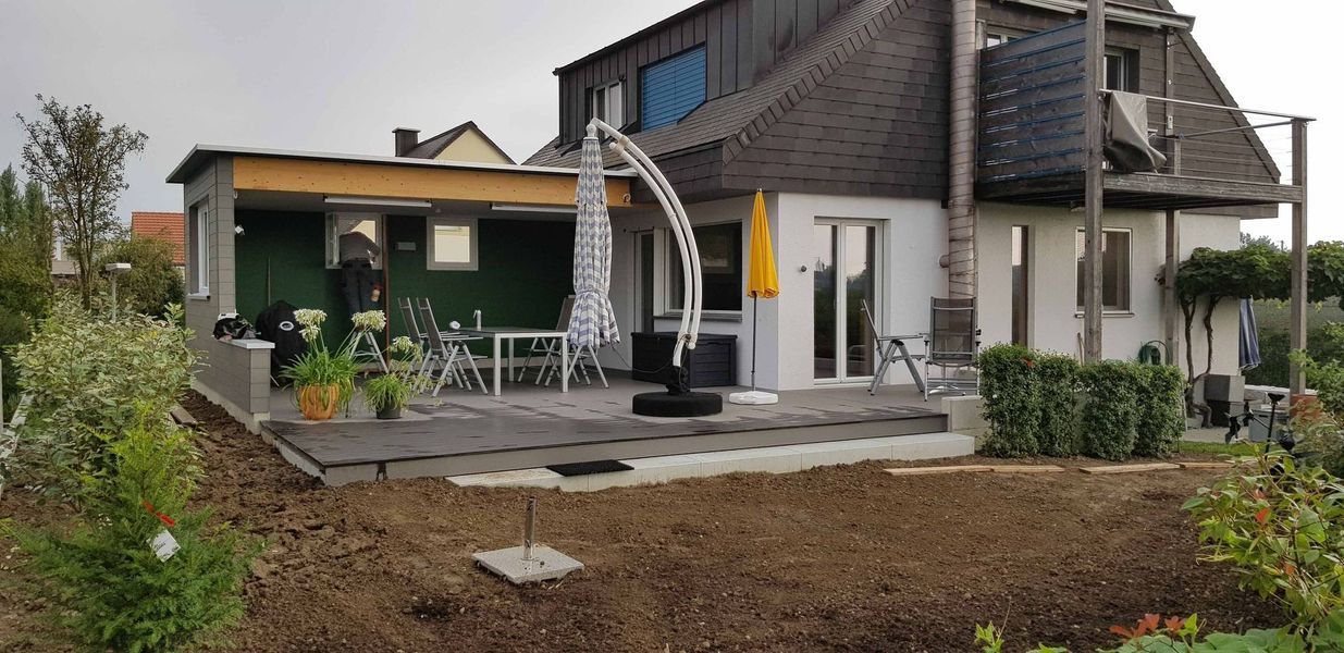 Ein grosses Haus mit Terrasse und Sonnenschirm davor. Foto von der Mannhart Holzbau AG