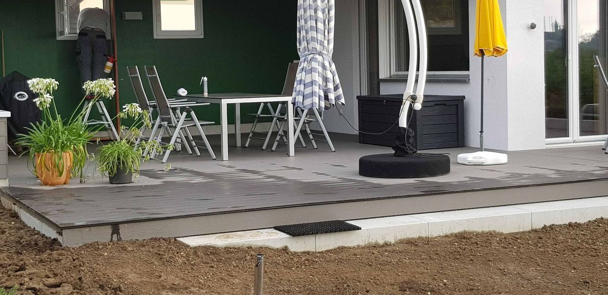 Eine Terrasse mit Tisch, Stühlen und Sonnenschirm vor einem Haus.