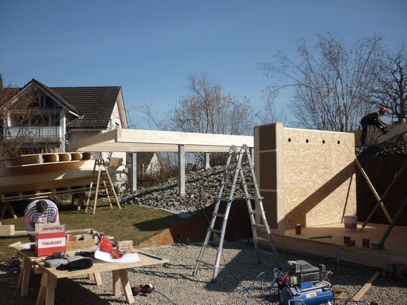 Ein Mann steht auf einer Leiter vor einem im Bau befindlichen Gebäude. Foto von der Mannhart Holzbau AG