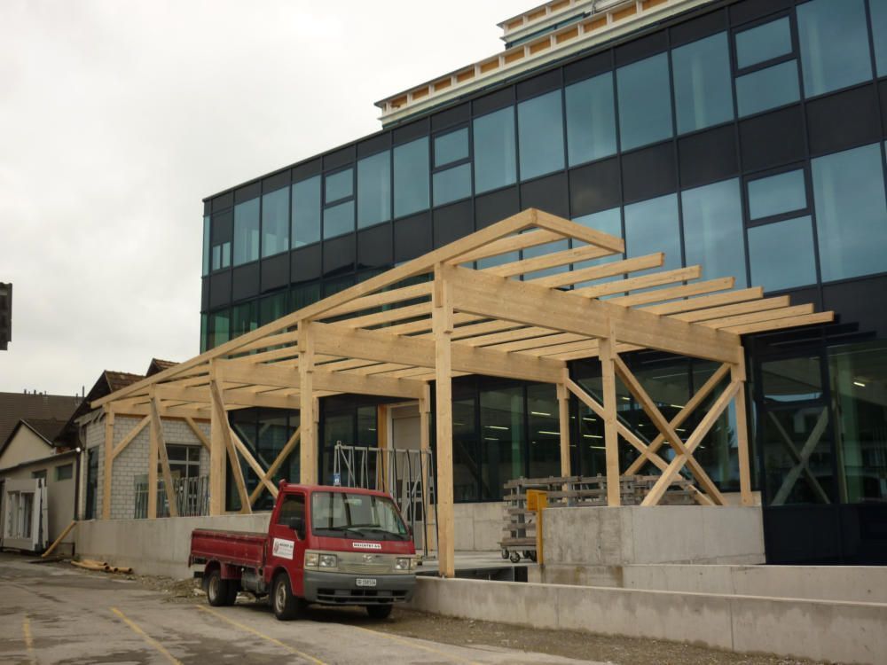 Ein roter Lkw steht vor einem im Bau befindlichen Gebäude. Foto von der Mannhart Holzbau AG