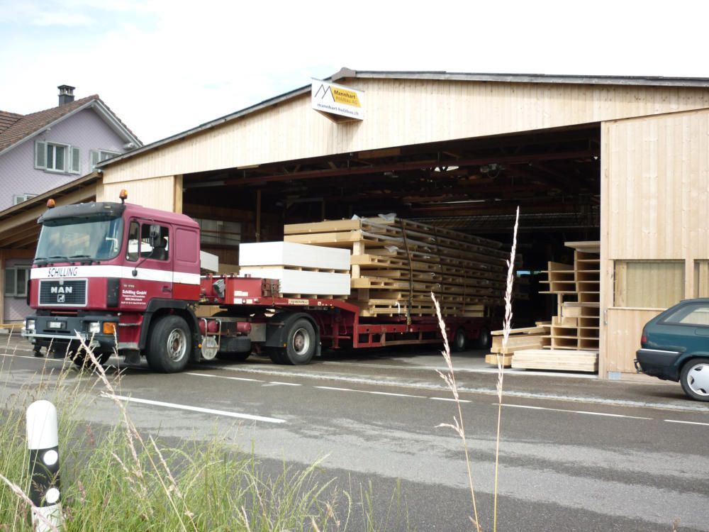 Ein rot-weisser Lkw steht vor einem Gebäude. Foto von der Mannhart Holzbau AG