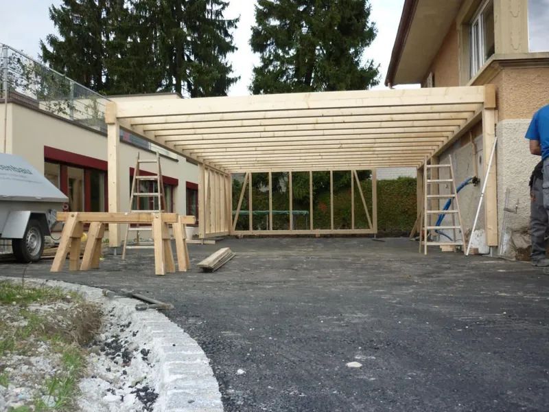 Vor einem Haus wird ein Holzcarport errichtet. Foto von der Mannhart Holzbau AG