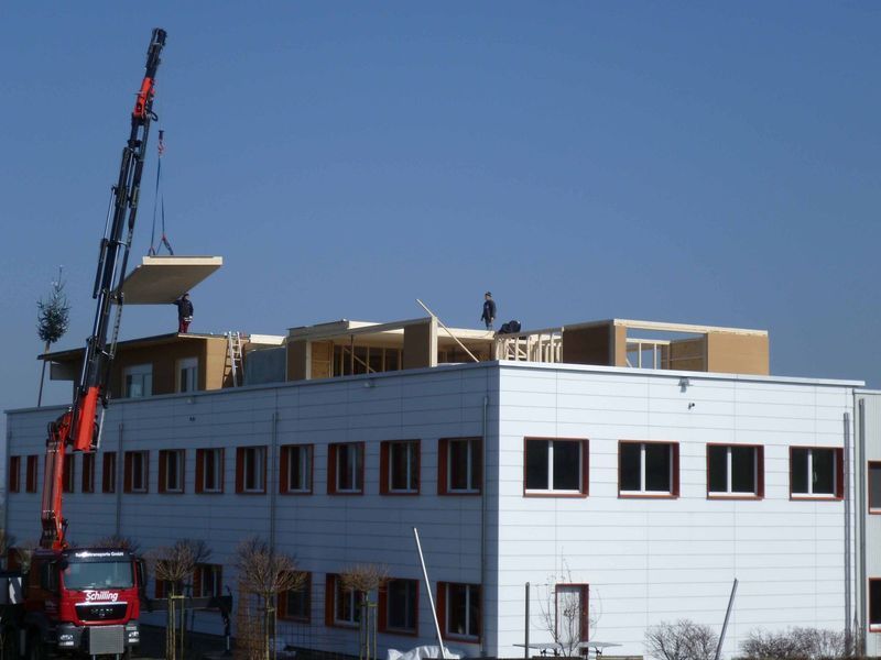 Ein Kran hebt ein Stück Holz auf ein Gebäude