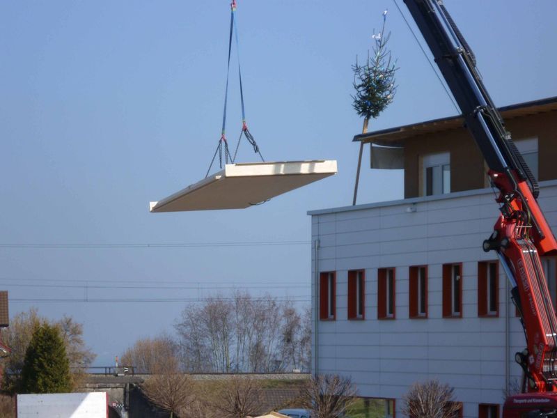 Ein Kran hebt ein Stück Holz über ein Gebäude
